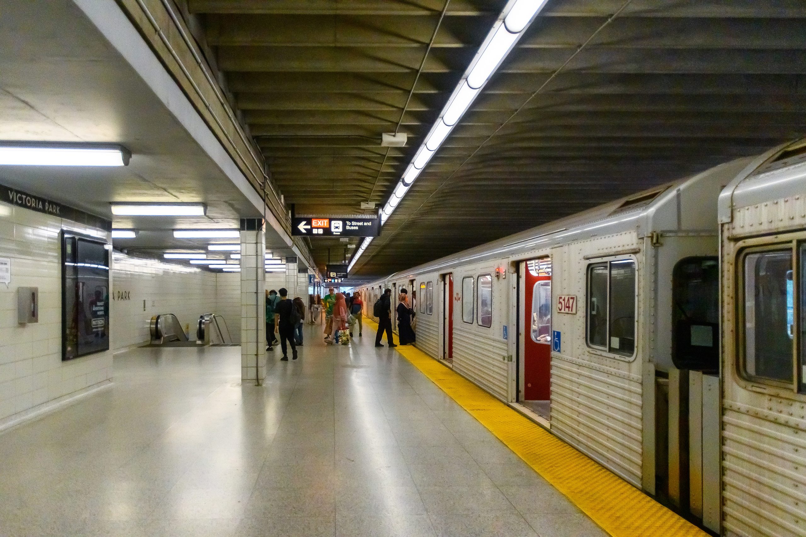 A Toronto subway train opens its door at a station. From a distance, passengers are seen exiting and embarking the train.