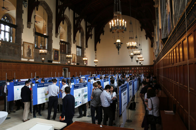 People in a great hall gathering around various symposium poster boards.